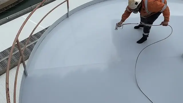 Technician applying NanoPrep by spray to the roof of a large steel storage tank