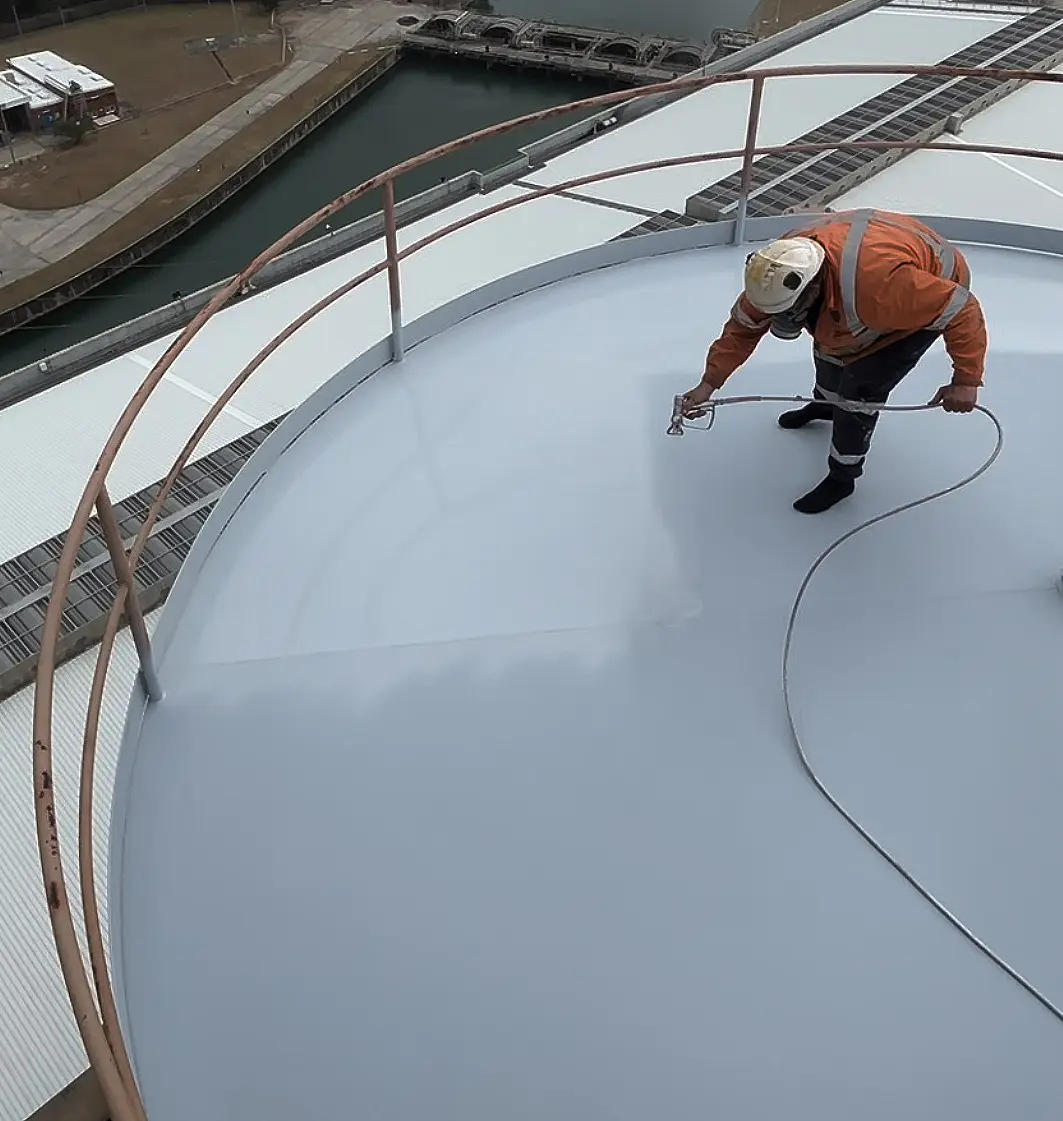 Technician applying NanoPrep by spray to the roof of a large steel storage tank